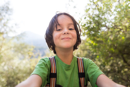 A child takes a selfie on the background of the forest, The boy is photographed on a smartphone, Smiling kid walks in the park.の写真素材
