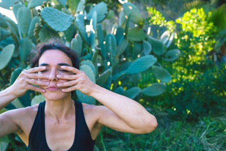 Woman does self-massage of the face, The girl practices yoga on the green grass on a background of green trees, A woman performs asanas at sunset, Meditation in nature, Female fingers on the face.の写真素材