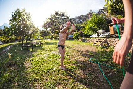 Boy drenched in water on a hot sunny day, Mother sprays a child with a hose in the courtyard of the house, Entertainment on vacation, The emotions of a child, Children's fun.の写真素材