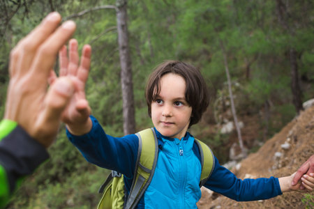 A boy with a backpack climbed to the top of the mountain and gives five, Traveling with children,...