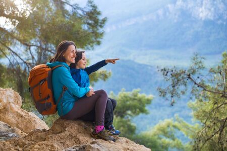 The boy and his mother are sitting on the top of the mountain. A woman is traveling with child. Boy with his mother looking at the mountains. Travel with backpacks. Hike and climb with kids.の写真素材