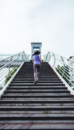 A woman runs up the stairs. Running training in the city. Jogging. Reaching the goal. The desire for...