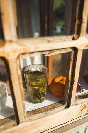A glass with herbal tea stands on the windowsill of an old wooden house. Green tea and orange near the window. A cup of hot drink.の写真素材