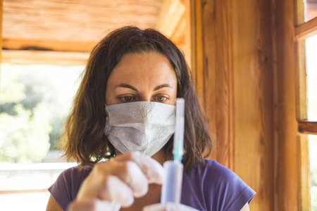 Woman in a protective mask is preparing to give an injection to the patient, The doctor holds a syringe, The treatment of the disease, Virus protection, Quarantine.の写真素材