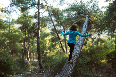 A woman walks along the trunk of a fallen tree in the forest. Girl catches balance. Walk through the...