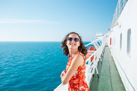 A woman is sailing on a cruise ship, a girl is standing near the fence on a ship and looking at the sea, traveling by ferry, a brunette in a summer dress admires the ocean.の写真素材