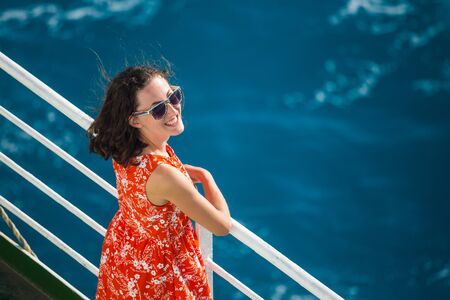 A woman is sailing on a cruise ship, a girl is standing near the fence on a ship and looking at the sea, traveling by ferry, a brunette in a summer dress admires the ocean.の写真素材