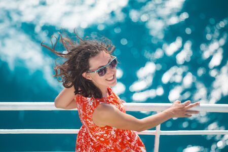 A woman is sailing on a cruise ship, a girl is standing near the fence on a ship and looking at the sea, traveling by ferry, a brunette in a summer dress admires the ocean.の写真素材