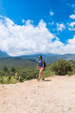 A woman with a backpack stands on top of a mountain and admires the beauty of a mountain valley, The girl travels to beautiful places, Reaching the goal. Beautiful landscape.の写真素材