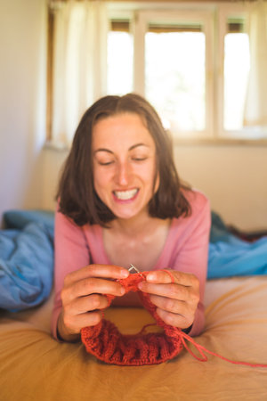 Woman knits while lying on the bed, Women's hands knit a hat, The girl is engaged in creativity...