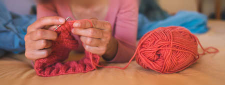 Woman knits while lying on the bed, Women's hands knit a hat, The girl is engaged in creativity during quarantine, Handmade, Favorite home hobby.の写真素材