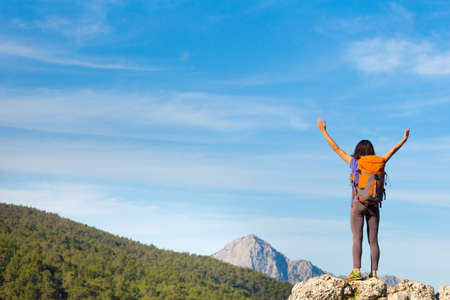 A woman with a backpack stands on top of a mountain and admires the beauty of a mountain valley, The girl travels to beautiful places, Reaching the goal. Beautiful landscape.の写真素材