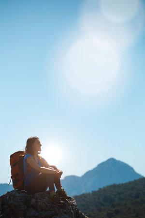 A woman with a backpack stands on top of a mountain and admires the beauty of a mountain valley, The girl travels to beautiful places, Reaching the goal. Beautiful landscape.の写真素材