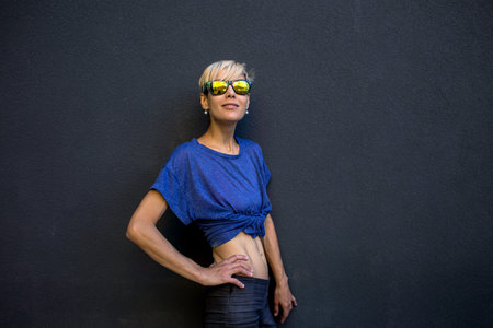 A girl with short hair stands against a dark gray wall, portrait of a blonde in sunglasses, a sexy...