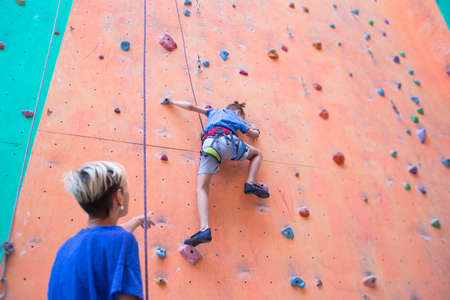 A coach teaches a child, a woman is belaying her son, a boy and his mother train together, children's training climbing, a boy climbs the wall, climbing gymの写真素材