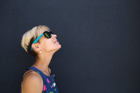 A girl with short hair stands against a dark gray wall, portrait of a blonde in sunglasses, a sexy...