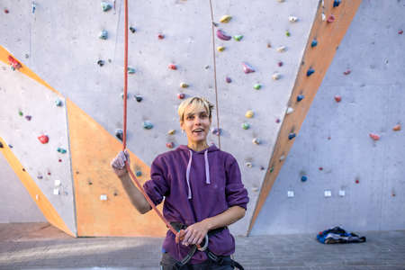 A girl trains on a climbing wall, happy woman climbed a route, preparation for overcoming a route in a climbing gym, equipment for belaying, a safety rope.の写真素材