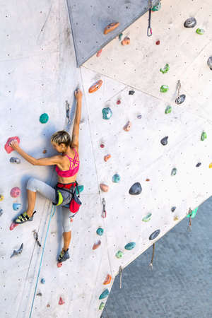 A woman climbs a climbing wall, a climber is training on artificial terrain, rock climbing in the city, a strong girl, sports in the city, safety in extreme sports.の写真素材