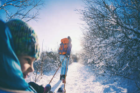A woman pulls a sled with a child. Mother walks with her son through a snowy forest. Winter walk in the park. The boy rides on a sled. Winter activities with children. Fisheye lens.の写真素材
