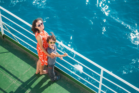 The family is sailing on a cruise ship, a mother with son are standing at the fence on the ship and...