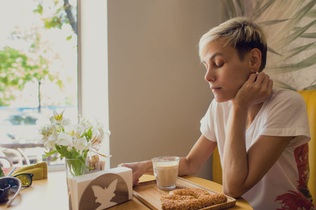 A woman is sitting in a coffee shop, a cappuccino in a glass, morning coffee, a blonde girl with short hair.の写真素材