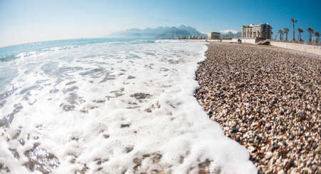 Turkish beach without people. Mediterranean Sea in Turkey. Ocean waves and coastal sand. Resort on the background of mountains and sky. Deserted beach.の写真素材