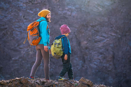 A woman is traveling with a child. Mom and son in the mountains. Climb to the top of the mountain with children. The boy with the backpack climbed to the top. Active vacations.の写真素材