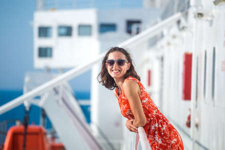 A woman is sailing on a cruise ship, a girl is standing near the fence on a ship and looking at the sea, traveling by ferry, a brunette in a summer dress admires the ocean.の写真素材