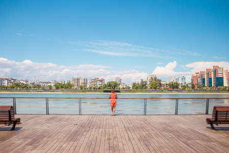 A girl in a dress walks on the promenade of Antalya, a woman stands on the banks of the river and looks at the water, the resort city of Turkey.の写真素材