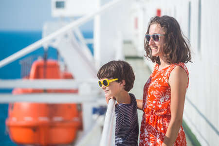 A woman is sailing on a cruise ship with her child, a girl is standing at the fence on the ship and looking at the sea, traveling by ferry, a boy and his mother are enjoying the ocean.の写真素材