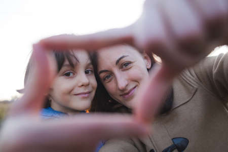 Child with mother folded fingers in the shape of a heart, Boy kisses and hugs mom, a portrait of a smiling woman, happy motherhoodの写真素材