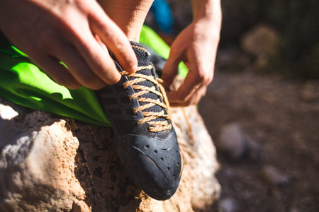 Rock climber puts on climbing shoes and ties shoelaces. A girl sits on a stone and puts on climbing...