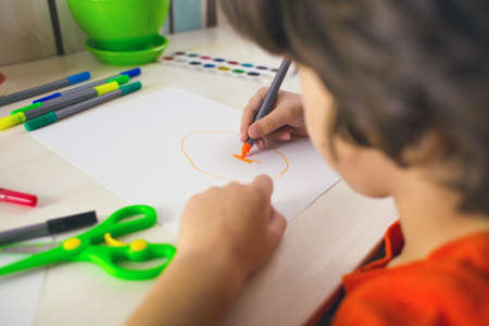 The boy draws with felt-tip pens on paper, the child is engaged in creativity, the child does his homework.の写真素材