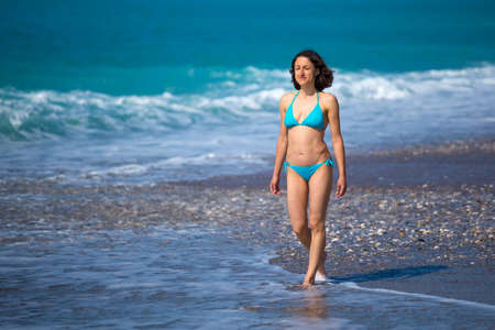 A woman in a swimsuit is walking along the sea waves, Turkish girl on the beach of Antalya, A brunette is walking along the beach, Holidays in Turkey.の写真素材