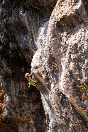 A young athlete climbs a rock, a climber trains on natural terrain, a man trains strength and endurance, rock climbing for children and teenagers.の写真素材
