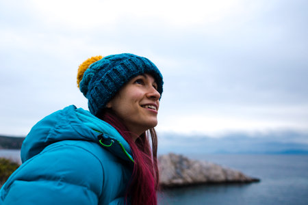 Portrait of a girl with red hair in a warm hat on the seashore. vacation at sea in the cold season....