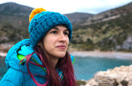 Portrait of a girl with red hair in a warm hat on the seashore. vacation at sea in the cold season....