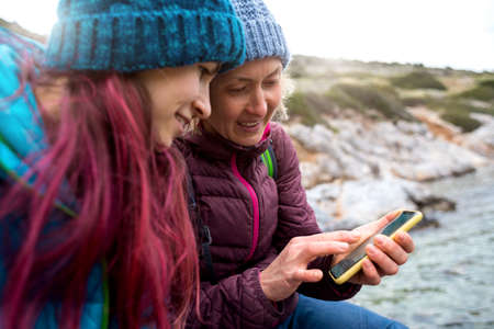 two girls travel and plan a route using the phone. mom and daughter went out for a walk in the cold season. couple having a good time outdoors.の写真素材
