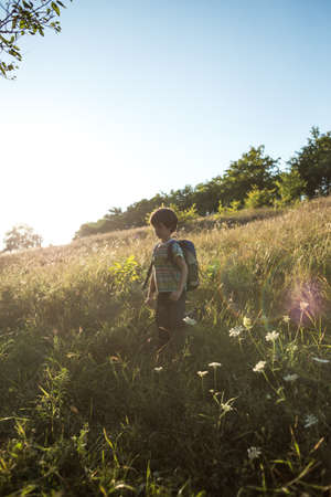 A boy with a backpack walks in the meadow, a child explores wildlife, a kid stands alone among the trees, a portrait of a boy.の写真素材