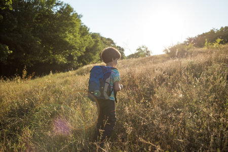 A boy with a backpack walks in the meadow, a child explores wildlife, a kid stands alone among the trees, a portrait of a boy.の写真素材
