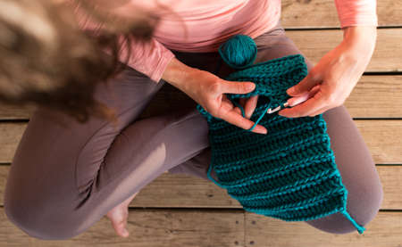 Woman crochets sitting in bed, Needlework during quarantine, The girl knits from thick blue yarn, Female hands close-up, Home hobby.の写真素材