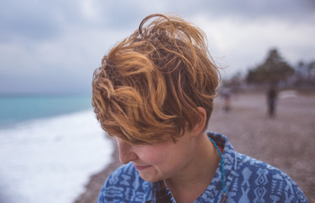 Portrait of a red-haired girl with freckles, a woman with short hair, wind in her hair, a walk along the coast, smiling girl on the beach.の写真素材
