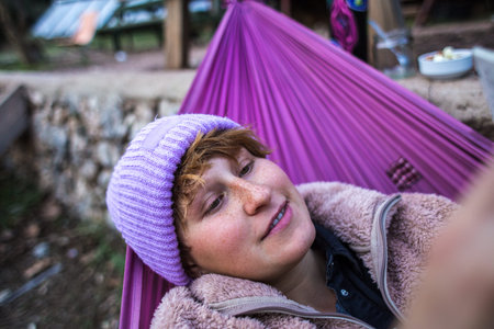 Red-haired girl with freckles lies in a hammock, portrait of a woman in a hat lying in a hammock,...