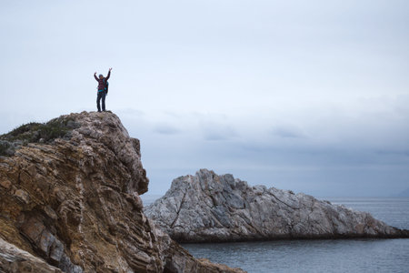 girl with a backpack stands on a mountain by the sea. the traveler looks at the sea, standing on the...