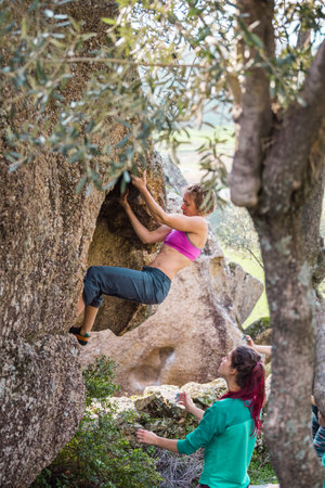 Friends go in for sports in nature, bouldering on rocks, girl climbs a big stone, woman is belayng partner, outdoor recreation, bouldering on the boulders of Lake Bafaの写真素材