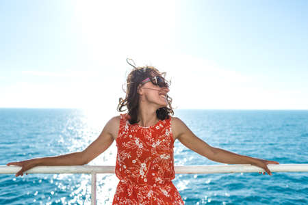 happy girl in a red sundress floats on the ship. summer ocean cruise. summer rest.の写真素材