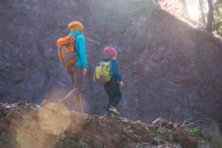 A woman is traveling with a child. Mom and son in the mountains. Climb to the top of the mountain with children. The boy with the backpack climbed to the top. Active vacations.の写真素材