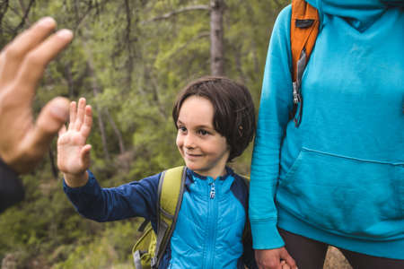 A boy with a backpack walks through the forest with his parents, a child holds out his palm to give five, a trip with children, a boy gives his hand to dad.の写真素材