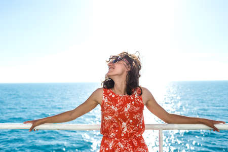 A woman is sailing on a cruise ship, a girl is standing near the fence on a ship and looking at the sea, traveling by ferry, a brunette in a summer dress admires the ocean.の写真素材