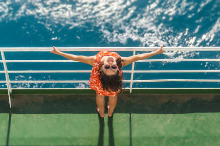 A woman is sailing on a ship, a girl in a summer dress is standing on the deck of a cruise ship, a journey across the ocean, a woman is sailing on a ferry and looks at the water.の写真素材
